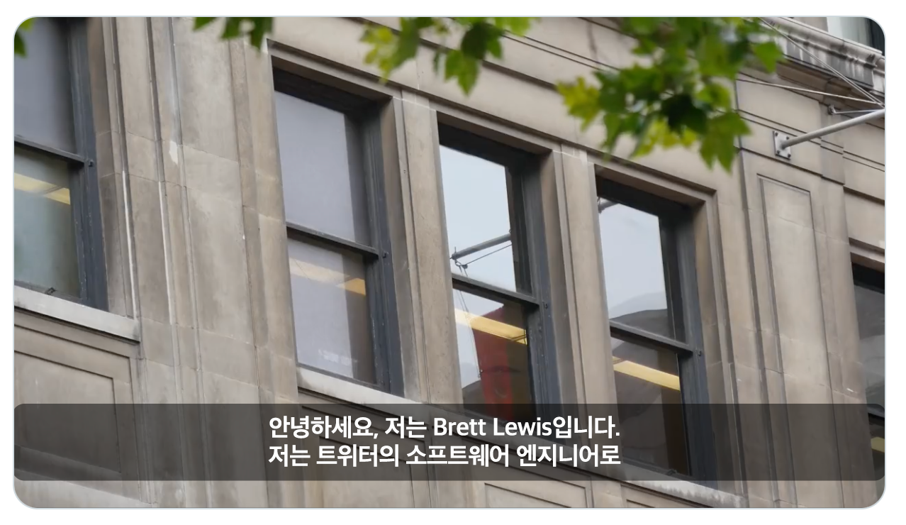 불투명한 검은색 배경에 흰색 텍스트로 표시된 캡션 시작 줄의 스크린샷. 동영상 화면에는 창문이 있는 건물의 측면 사진이 나타나 있다.